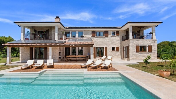 Une maison à deux étages avec une piscine, un espace salon extérieur et une façade en pierre.