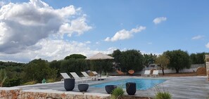 A poolside area with lounge chairs, a large umbrella, and a stone wall.