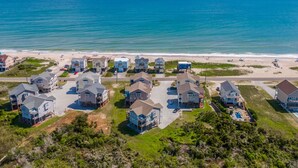 An aerial view of a coastal residential area with houses, a beach, and a clear blue sky. - Sunset Cove | Sound Views + Walk to the Beach! (North Topsail Beach)