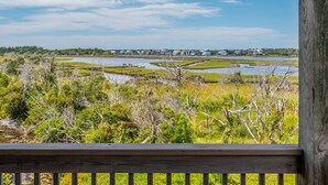 A view of a coastal area with a wooden deck, a river, and houses in the background. - Sunset Cove | Sound Views + Walk to the Beach! (North Topsail Beach)
