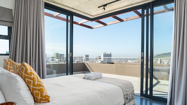 Ein modernes Hotelzimmer mit einem großen Bett, Blick auf die Stadt und einem Balkon mit Glastür.