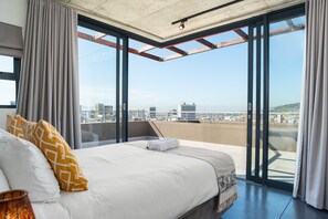 Habitación de hotel moderna con una cama grande, vistas a la ciudad y un balcón con puerta de vidrio.