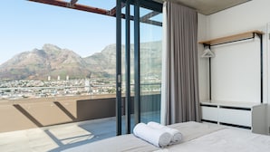 Ein Hotelzimmer mit großem Fenster, einem Bett mit zusammengerollten Handtüchern, einem Holzboden und einem weißen Schreibtisch.