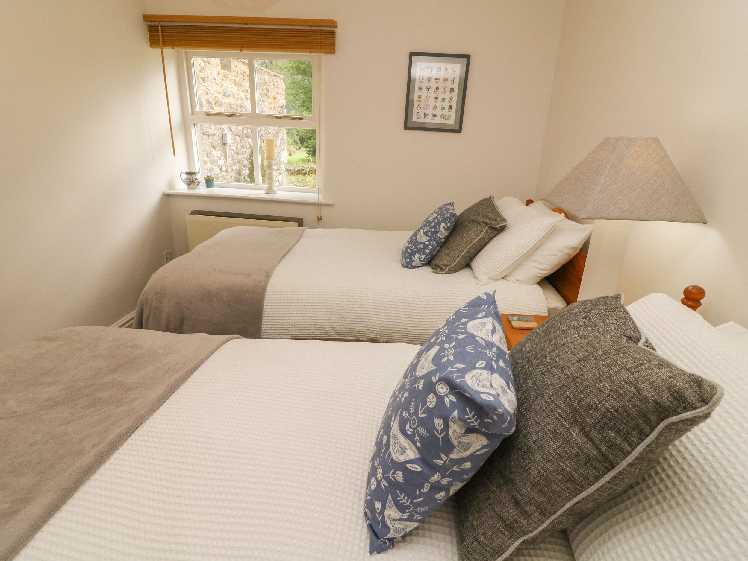 Una camera da letto con due letti, una finestra con tende, un quadro appeso al muro e una lampada da comodino.