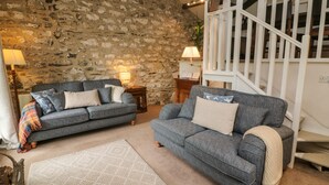 A cozy living room with two grey sofas, a stone wall, and a wooden staircase. - Nuthatch Cottage (Skipton)