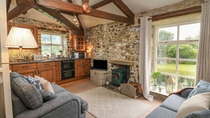 A cozy living room with a stone fireplace, wooden beams, and a large window overlooking a garden. - Nuthatch Cottage (Skipton)
