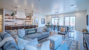 A modern living room with a sectional sofa, a dining area, and a kitchen with open shelving. - Arcadia 53 | DOG FRIENDLY * PRIVATE Hot Tub * Arcade Games * Sleeps 21 (Santa Clara)