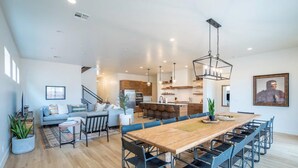 A modern open-plan living area with a dining table, sofas, and a kitchen in the background. - Arcadia 53 | DOG FRIENDLY * PRIVATE Hot Tub * Arcade Games * Sleeps 21 (Santa Clara)