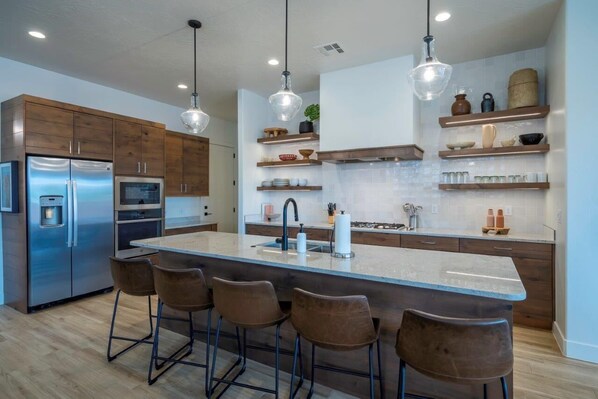 Een moderne keuken met een centraal eiland, barkrukken, roestvrijstalen apparatuur en houten keukenkastjes.
