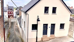 A two-story building with a dark roof, white walls, and a black door. There is a narrow street in front of the building, and a satellite dish is visible on the left side. - Louise's Cottage, downtown Saint Valery sur Somme (Saint-Valery-sur-Somme)