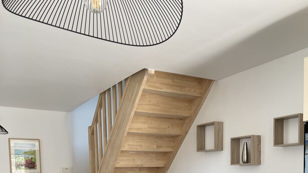 A modern living room with a wooden staircase, a grey sofa, two round tables, and a pendant light. - Louise's Cottage, downtown Saint Valery sur Somme (Saint-Valery-sur-Somme)