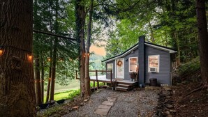 Une cabane dotée d’un porche, entourée d’arbres et bordée d’un chemin de gravier.
