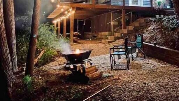 Une maison à deux étages dotée d’une terrasse, entourée d’arbres et illuminée de guirlandes lumineuses.