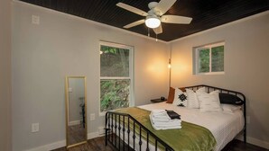 Une chambre à coucher comprenant un lit, un ventilateur de plafond, deux fenêtres, un miroir et une table de chevet.