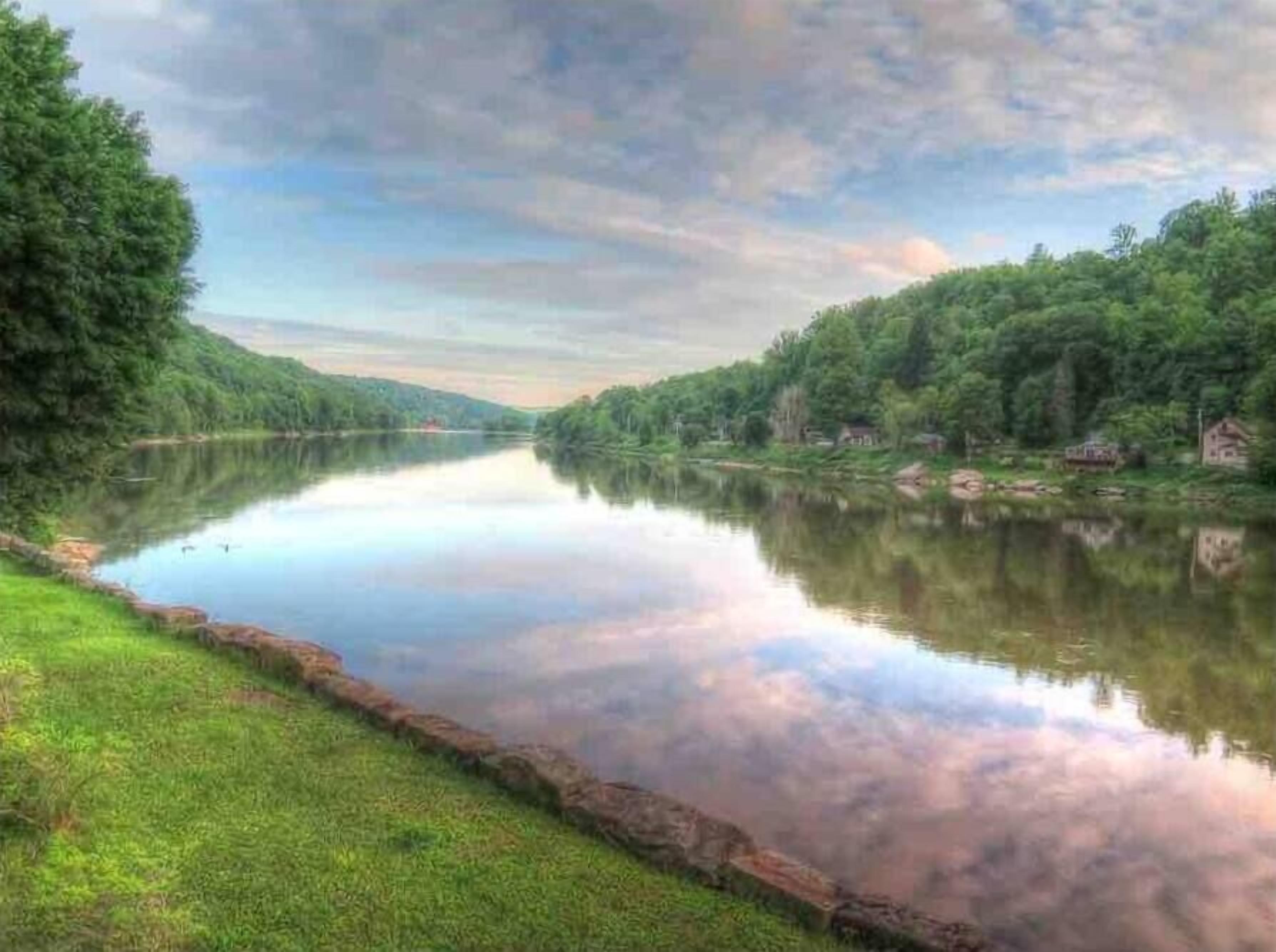 A calm river with a grassy bank and trees on both sides.