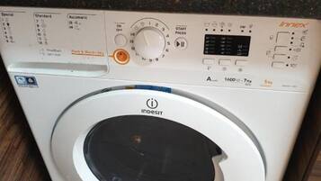 Una rentadora de càrrega frontal Indesit amb un panell de control, una caixeta per a pa vermella i un brollador vermell a la superfície de treball.