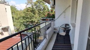 A balcony with a small table and chairs, a metal railing, and a view of trees and buildings. - Apartment Lozenets, Sofia, Bulgaria (Sofia)