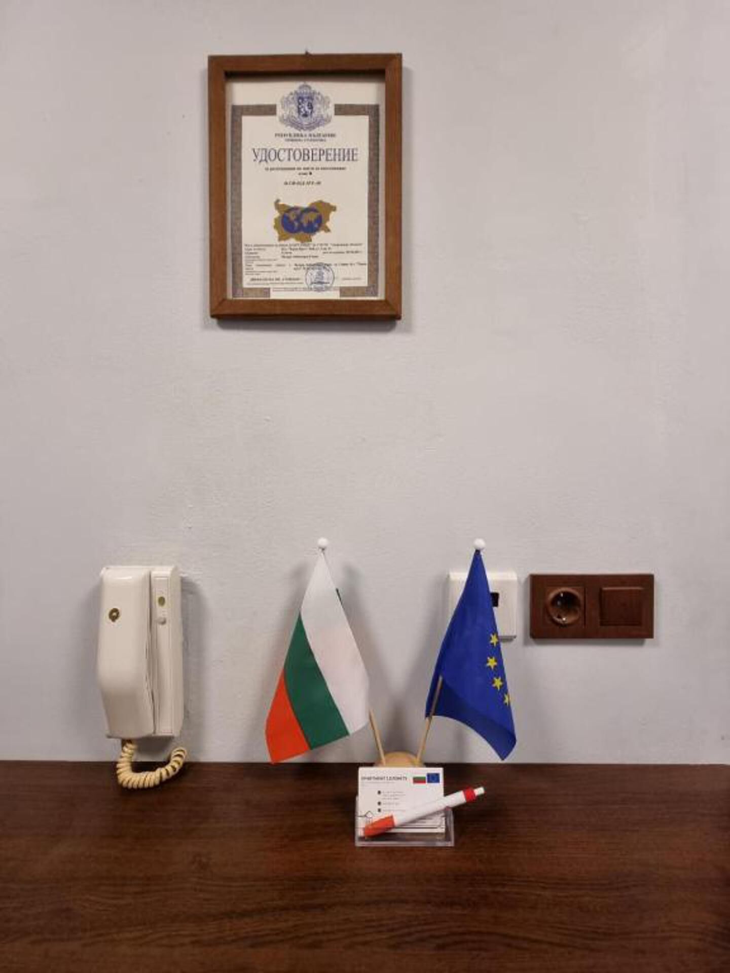 Un certificado enmarcado en la pared, un teléfono y dos banderas sobre un escritorio.