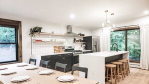 Ett modernt kök med en central köksö, barstolar och ett matbord med plats för sex personer.