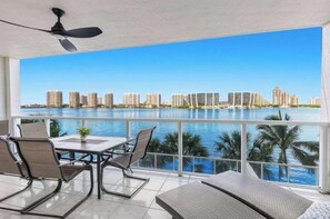 A balcony with a table and chairs, overlooking a water body and city skyline. - Le Marina Bay 409  	STR-03586 (Sunny Isles Beach)