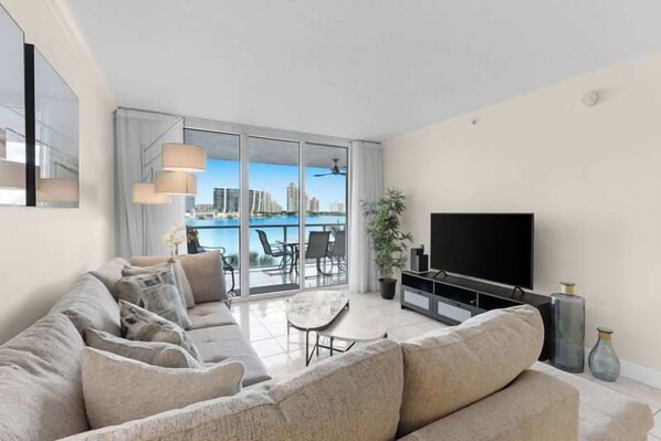 A modern living room with a sofa set, a flat-screen TV, and a dining area with a table and chairs. - Le Marina Bay 409  	STR-03586 (Sunny Isles Beach)