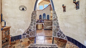 Un arco de piedra que da acceso a una sala de estar con chimenea, un aparador de madera y un letrero de bienvenida.