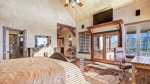 Una habitación amplia con una cama grande, techo de madera y vistas a través de un ventanal.