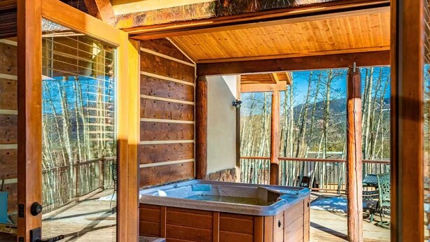 Una cabaña de madera con jacuzzi, paredes de madera y vista a los árboles.