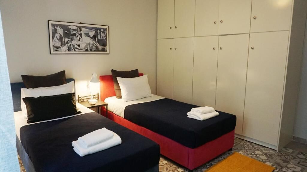 A hotel room with two beds, a wardrobe, a nightstand, and a lamp.
