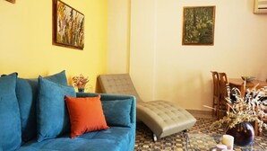 A living room with a blue sofa, a grey ottoman, and a dining table with chairs. - A few Steps from Syntagma and Plaka (Athens)