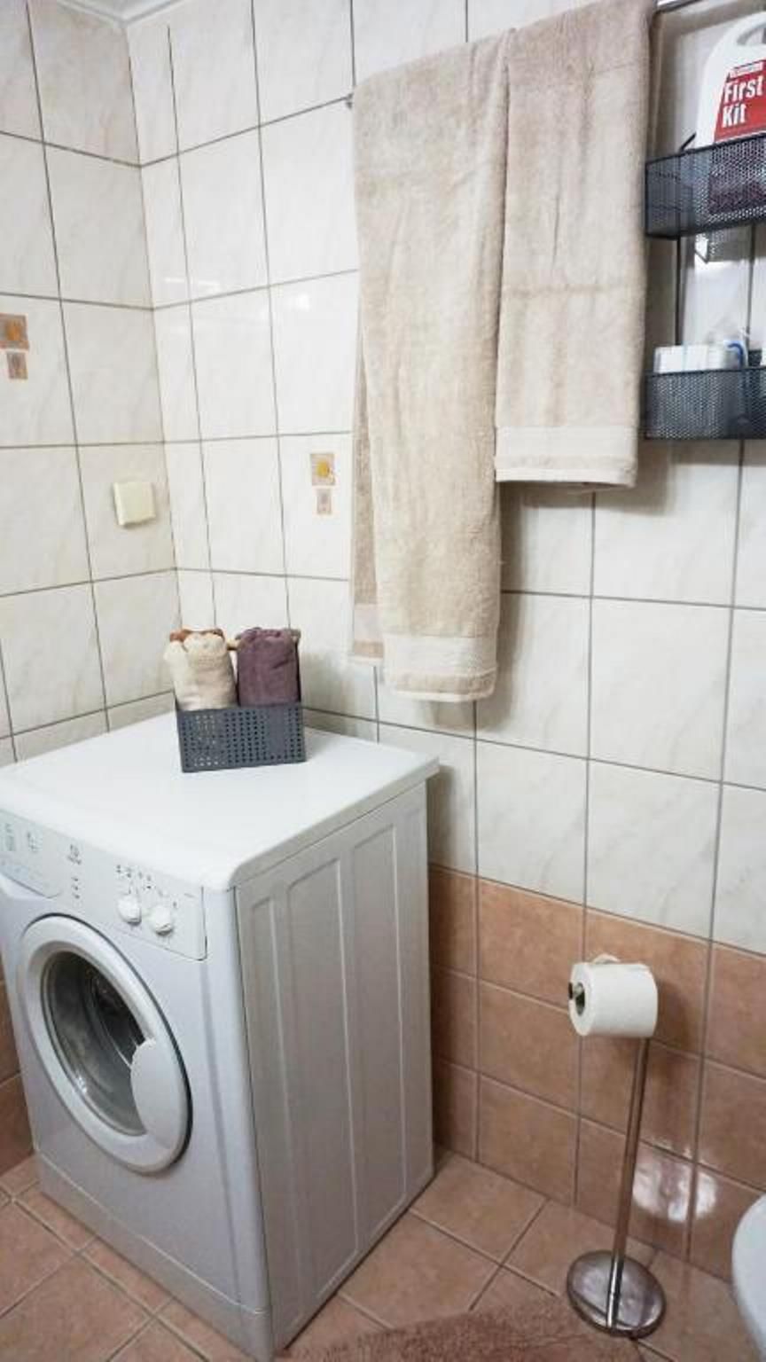 Ein Waschbereich mit Waschmaschine, Wäschekorb und Handtüchern an einem Gestell.