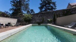Una piscina rectangular con agua cristalina, rodeada por un muro de piedra y una terraza de madera.