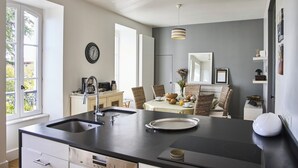 Una cocina moderna con una isla grande, un comedor con mesa puesta para cuatro y vistas al exterior a través de amplios ventanales.