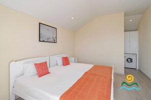 A bedroom with a bed, pillows, a framed picture, a washing machine, and a cabinet. - Peaceful, great for walks | SeaView Apartment (Prazeres)