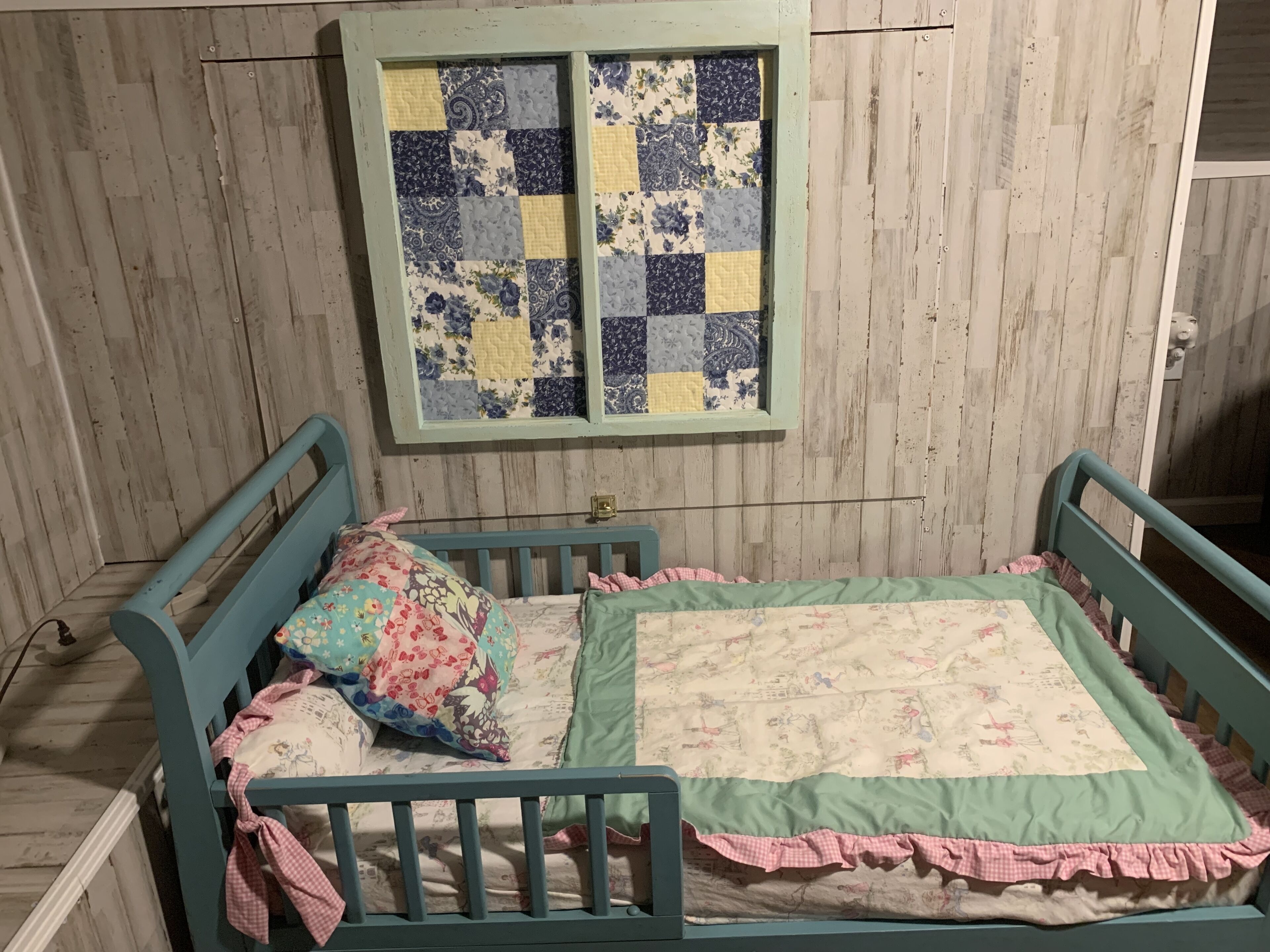 Une petite pièce chaleureuse, dotée d’un plancher en bois, d’un lit simple recouvert d’une couette à motifs floraux et d’une fenêtre à carreaux située au-dessus du lit.