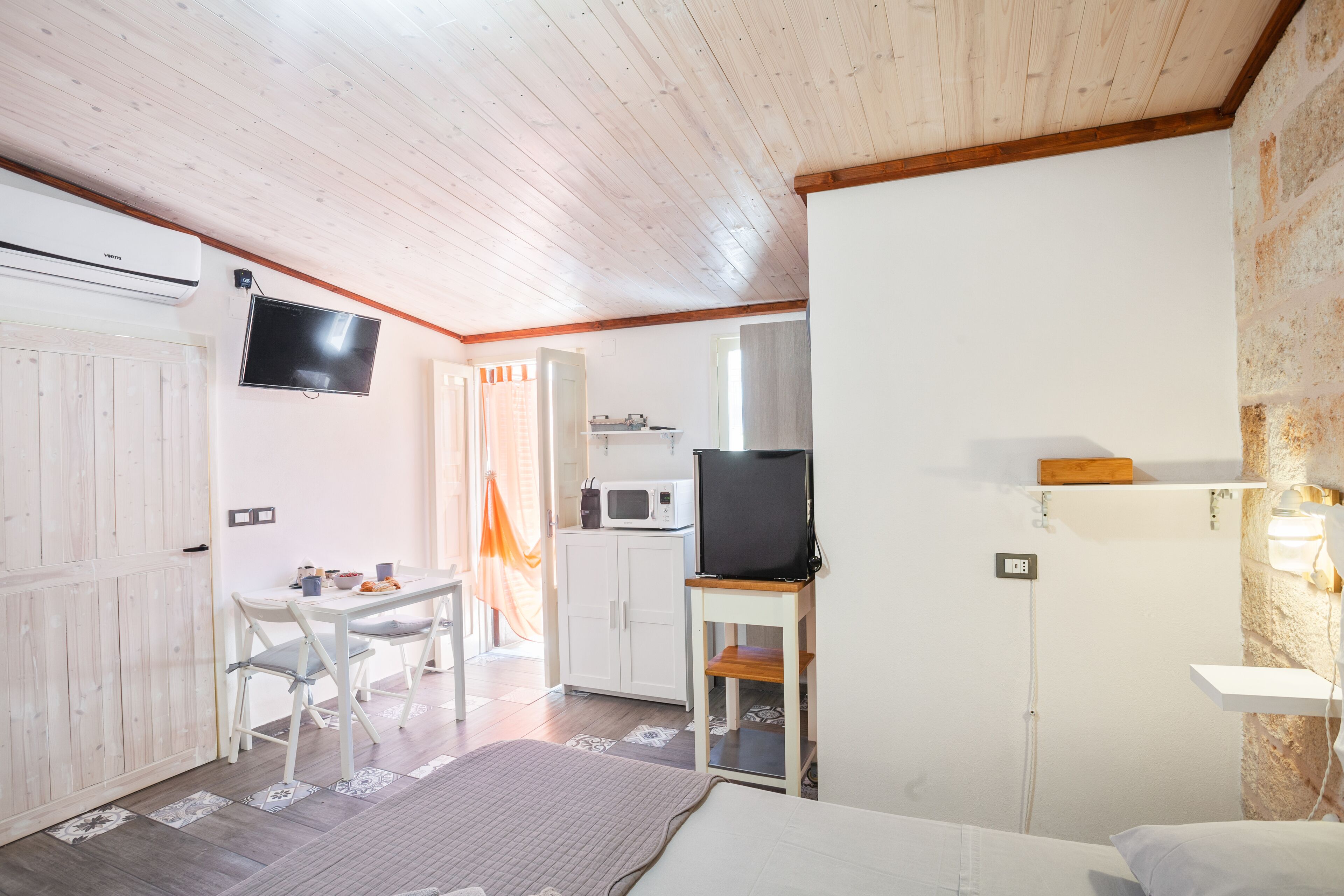 A room with a bed, a TV, a microwave, a dining table with chairs, and a wardrobe.