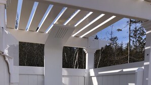 A portable outdoor shower with a white exterior, a metal frame, and a control panel with multiple buttons and a hose.