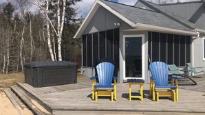 A wooden deck with two blue Adirondack chairs, a hot tub, and a covered area with a glass door.