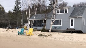 A beach house with a covered deck, outdoor seating, and a sandy beach area.
