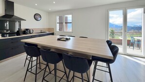 A modern kitchen with a large island, black chairs, and a view of the outdoors. - Comfortable Chalet - View of Lake Aiguebelette (La Motte-Servolex)