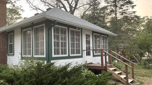 Un pequeño edificio de una sola planta con fachada verde y blanca, un porche delantero y una escalera de madera que conduce a la entrada.