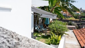 Un patio con dos sillones de descanso y una mesa, un toldo blanco y una planta en maceta.