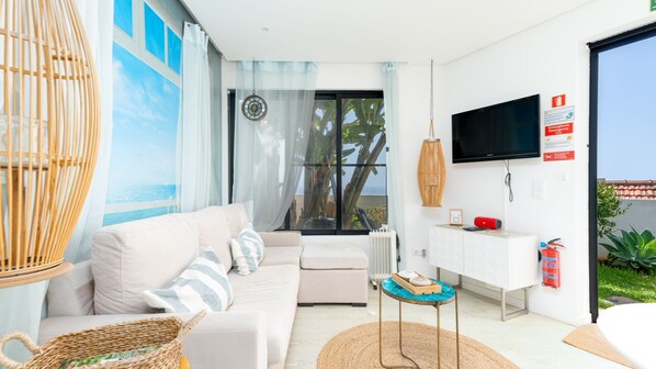 Una sala de estar moderna con un sofá, un televisor, una mesita y vistas al mar a través de amplios ventanales.