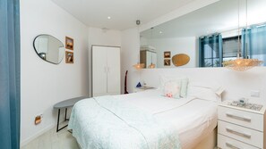A bedroom with a bed, bedside table, dresser, and a large mirror.