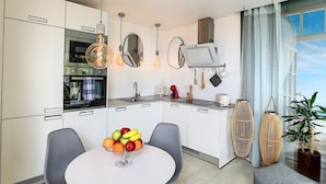 A modern kitchen with white cabinets, a round dining table with two chairs, a fruit bowl, and hanging light fixtures.