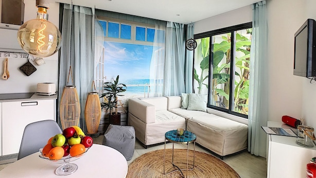 A modern living room with a view of the ocean, a dining area with fruit, and a cozy seating area.