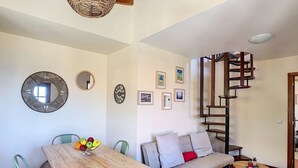 A dining area with a wooden table and chairs, a sofa, a small round table, and a spiral staircase. - Pôr do Sol by LovelyStay (Arco Da Calheta)