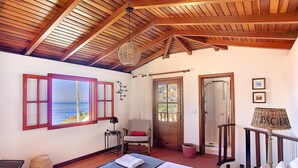 A room with a bed, a window with a view, a door, and a small table with a lamp. - Pôr do Sol by LovelyStay (Arco Da Calheta)