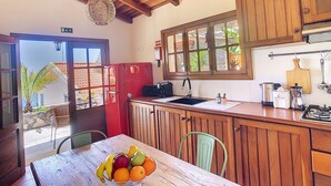 A kitchen with wooden cabinets, a red refrigerator, a sink, and a dining area with a table and chairs. - Pôr do Sol by LovelyStay (Arco Da Calheta)