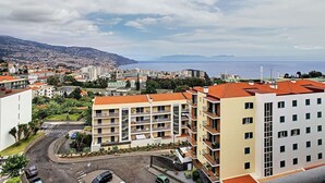 A coastal cityscape with a prominent apartment building featuring balconies and a view of the sea. - Gemini Apartment by LovelyStay (Funchal)